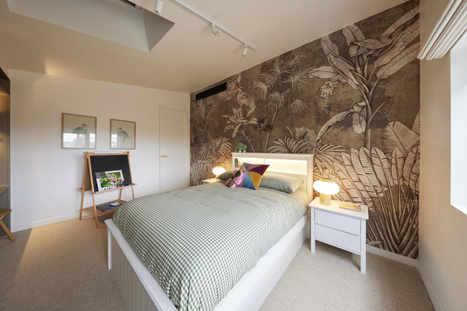 A wide shot of the room with a double bed in the middle, jungle themed wallpaper behind it, and a chalkboard on the left. 