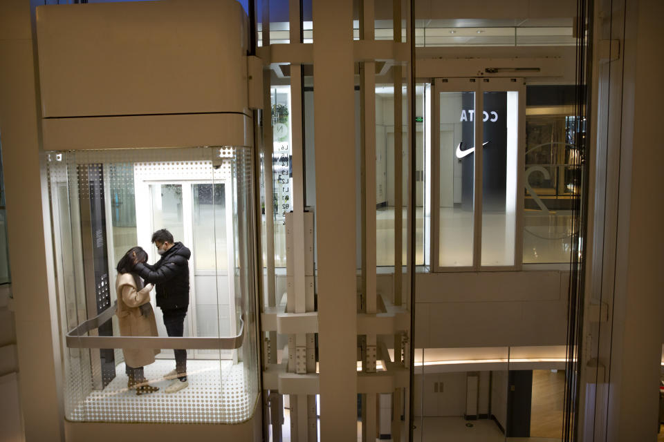 A couple wearing face masks ride an elevator at a nearly empty shopping mall in Beijing, Wednesday, Jan. 29, 2020. Fears of a virus outbreak have kept many indoors and at home in China's capital. Cultural landmarks such as the Great Wall and Forbidden City have closed their doors to visitors, nearly deserted shopping malls have reduced their operating hours, and restaurants that remain open draw just a handful of customers. (AP Photo/Mark Schiefelbein)