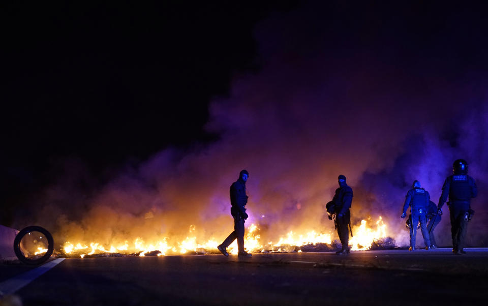 Police officers try to remove burning tires, set by demonstrators to block a highway in protest of the imprisonment of pro-independence political leaders during a general strike in Catalonia, Spain, Thursday, Feb. 21, 2019. (AP Photo/Daniel Cole)