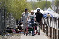 Pedestrians walk on a sidewalk next to a homeless encampment as temperatures continue to soar past 115-degrees Thursday, June 17, 2021, in Phoenix. (AP Photo/Ross D. Franklin)