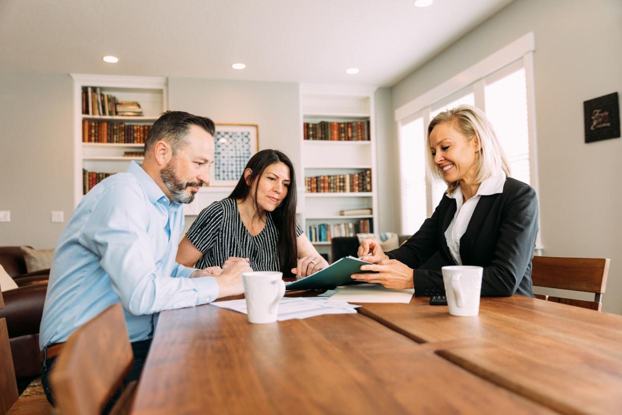 A female financial advisor and accountant meets with a married couple in their home to discuss investments and income. They are sitting at a table discussing savings, investments and taxes. Image taken in Utah, USA.