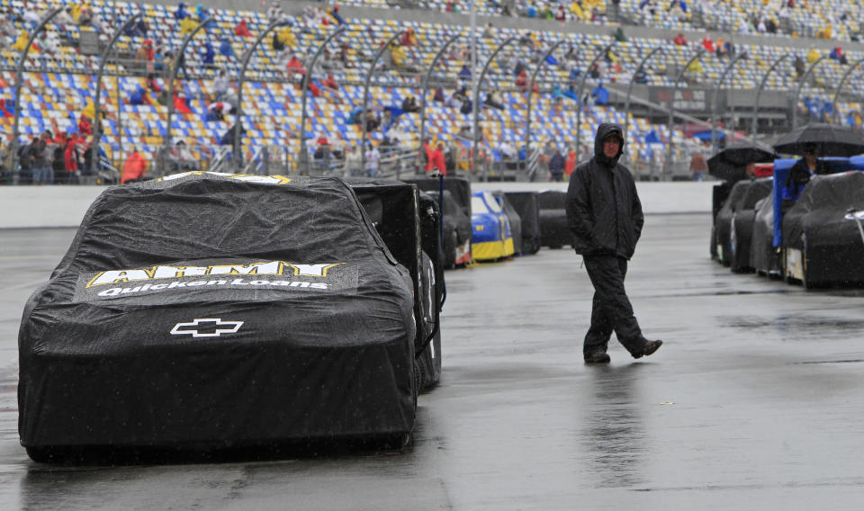 An crew member walks past race cars covered to protect them from the rain before the NASCAR Daytona 500 Sprint Cup series auto race at Daytona International Speedway in Daytona Beach, Fla., Sunday, Feb. 26, 2012. (AP Photo/John Raoux)