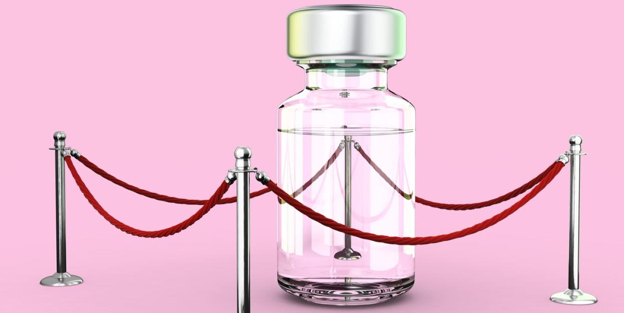 a bottle containing medical liquid stands alone inside a red roped area on a pale pink backdrop, low angle view