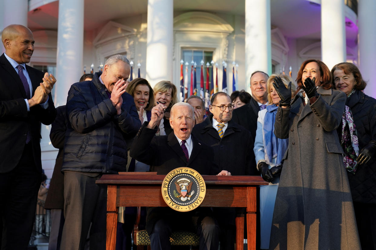 President Biden, surrounded by applauding Democratic officials, holds up his pen jubilantly after signing the Respect for Marriage Act in front of the White House.