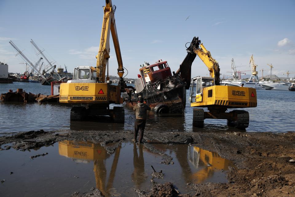 A worker takes photographs as heavy machinery destroys an abandoned boat on Salamina island, west of Athens, on Tuesday, Feb. 12, 2020. Greece this year is commemorating one of the greatest naval battles in ancient history at Salamis, where the invading Persian navy suffered a heavy defeat 2,500 years ago. But before the celebrations can start in earnest, authorities and private donors are leaning into a massive decluttering operation. They are clearing the coastline of dozens of sunken and partially sunken cargo ships, sailboats and other abandoned vessels. (AP Photo/Thanassis Stavrakis)