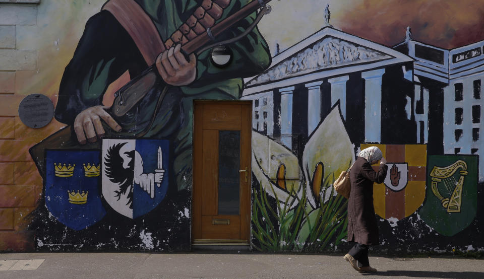 A woman adjusts her head scarf while walking past a Nationalist mural on the Falls Road in Belfast, Northern Ireland, Friday, March 24, 2017. (AP Photo/Alastair Grant)