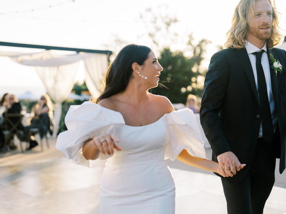 A bride and groom hold hands on the dance floor of their wedding.