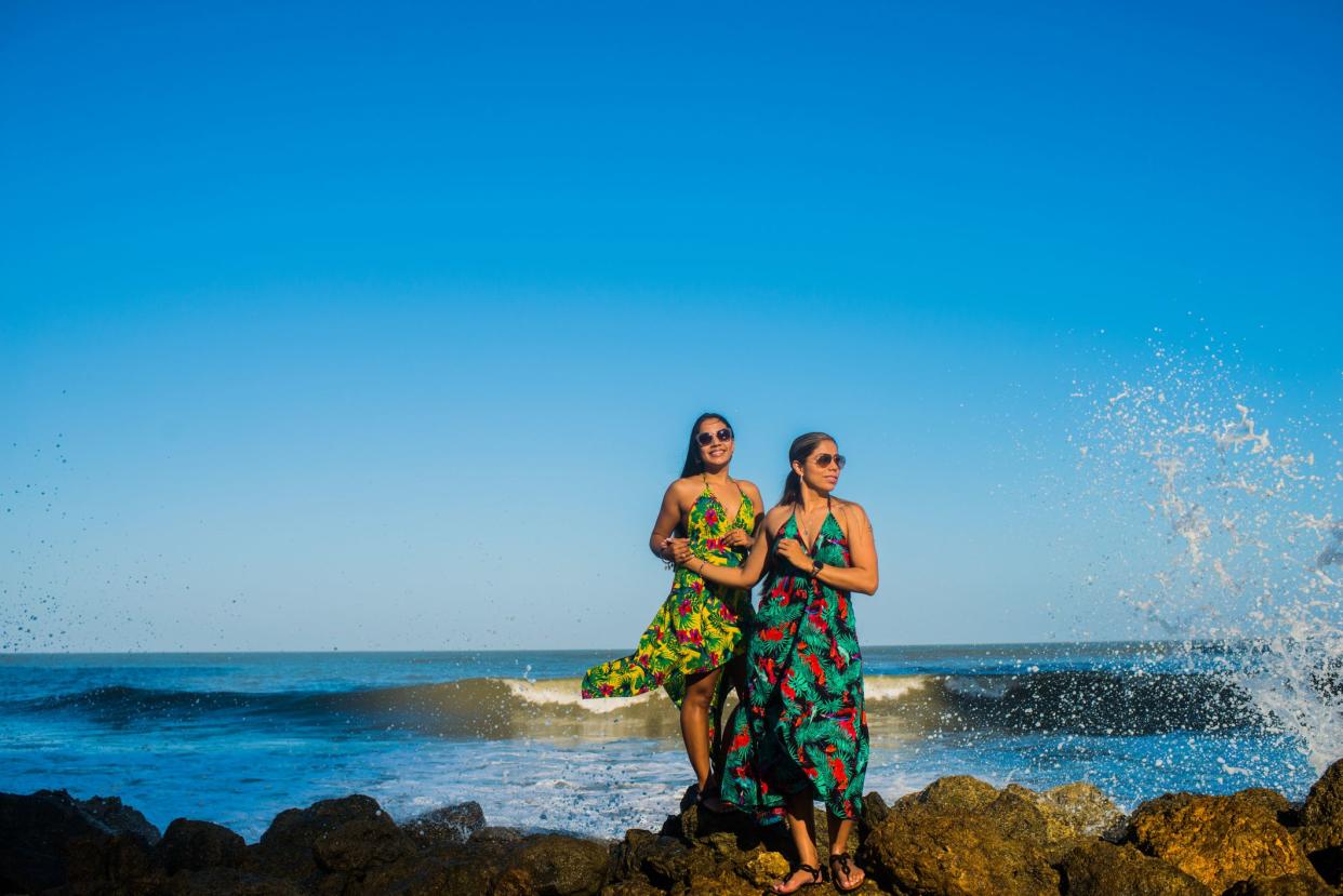 Portrait of two brides on their honeymoon strolling along the beach in their dresses.