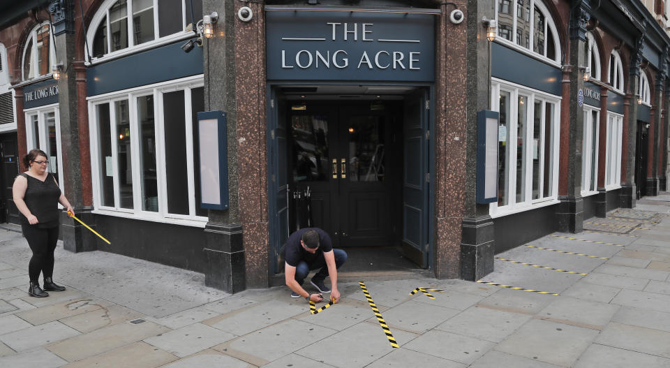 Employees mark the outside of a pub with tape for social distancing, prior to reopening, in London, Tuesday, June 30, 2020. Tuesday marked 100 days since Britain's Prime Minister Boris Johnson detailed a short list of reasons why individuals could leave their homes as he ordered the immediate closure of all shops selling non-essentials. (AP Photo/Frank Augstein)