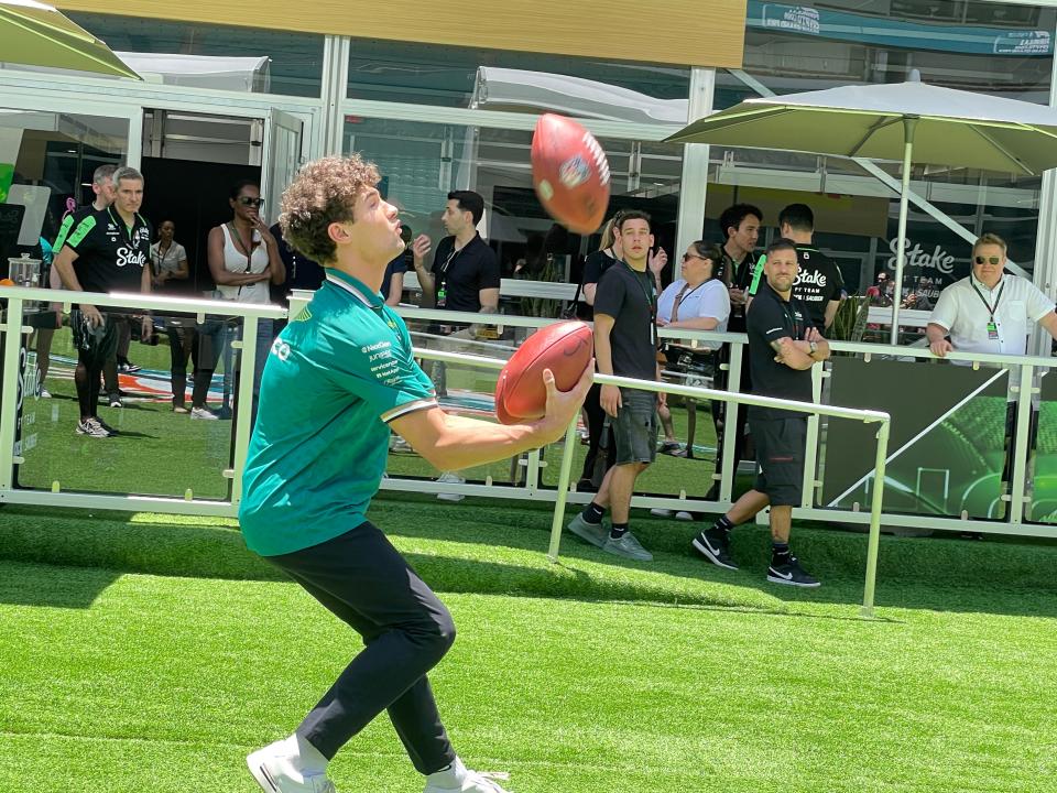 Jak Crawford, driver for Aston Martin in Formula 1, successfully hauls in a punt from a JUGS machine despite already holding a football in each hand.