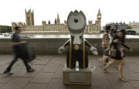 People walk by an Olympic mascot, painted in the likeness of a member of Parliament, across the River Thames from Parliament on Saturday, July 21, 2012, in London. The statue is one of 84 fiberglass sculptures of the mascots Wenlock or Mandeville that were painted by various artists and erected across the city for the 2012 London Olympic Games. (AP Photo/Charlie Riedel)