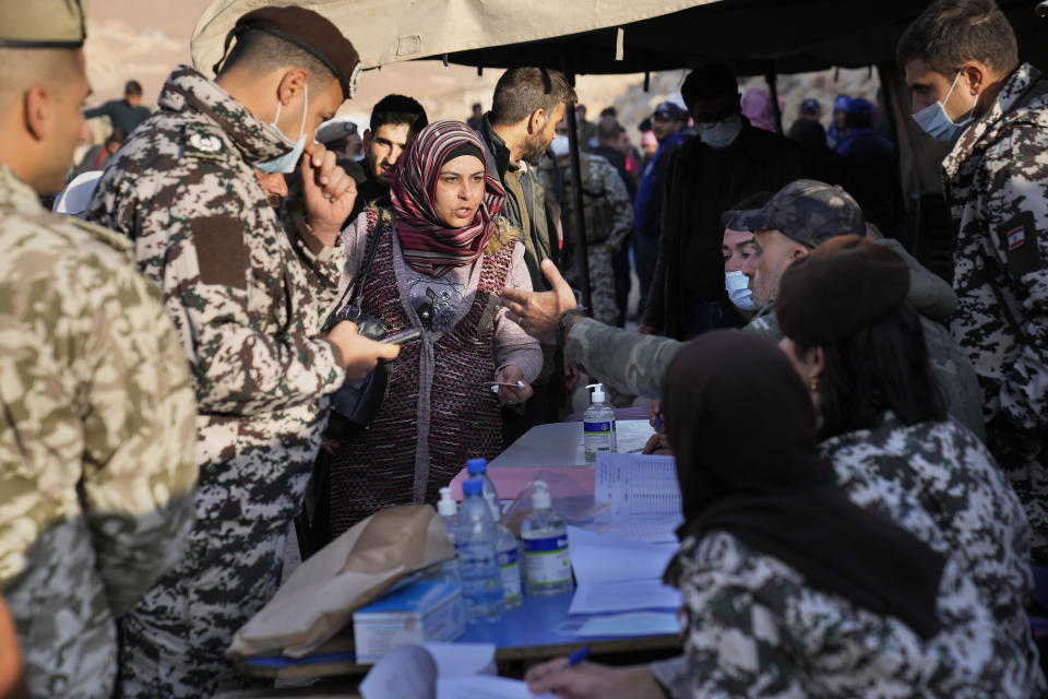 A Syrian refugee woman, center, checks her name with Lebanese General Security officers, at a gathering point where they prepare to cross the border back home to Syria, in the eastern Lebanese border town of Arsal, Lebanon, Wednesday, Oct. 26, 2022. Several hundred Syrian refugees boarded a convoy of trucks laden with mattresses, water and fuel tanks, bicycles – and, in one case, a goat – Wednesday morning in the remote Lebanese mountain town of Arsal in preparation to return back across the nearby border.(AP Photo/Hussein Malla)