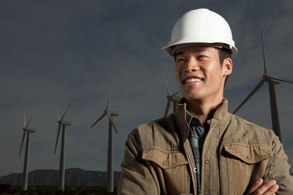 A man wearing a hard hat stands with wind turbines in the background