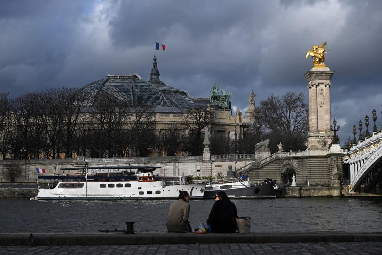 Des personnes assises le long de la Seine devant le Grand Palais, à Paris, le 11 janvier 2023. - EMMANUEL DUNAND / AFP