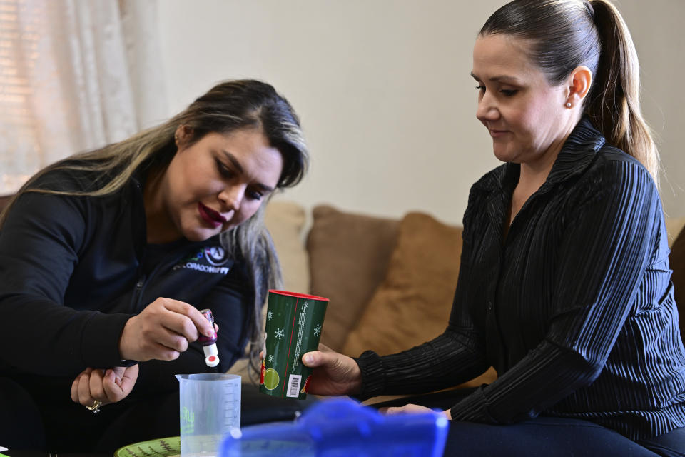 Instructor Mayra Ocampo, prepares materials for a science lesson to demonstrate to Isabel Valencia in Valencia's home in Pueblo, Colo., Wednesday, Feb. 28, 2024. Home visit programs have provided a lifeline for families, especially those for whom access to qualify early education is scarce or out of reach financially. The programs, which are set to expand with new federal support, are proven to help prepare children for school but have reached relatively few families. (AP Photo/Eric Lars Bakke)