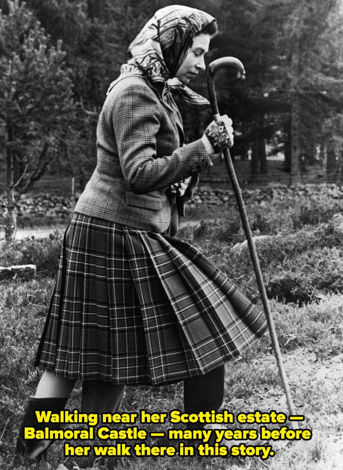 The Queen walking with a walking stick and wearing a scarf around her head and a plaid skirt