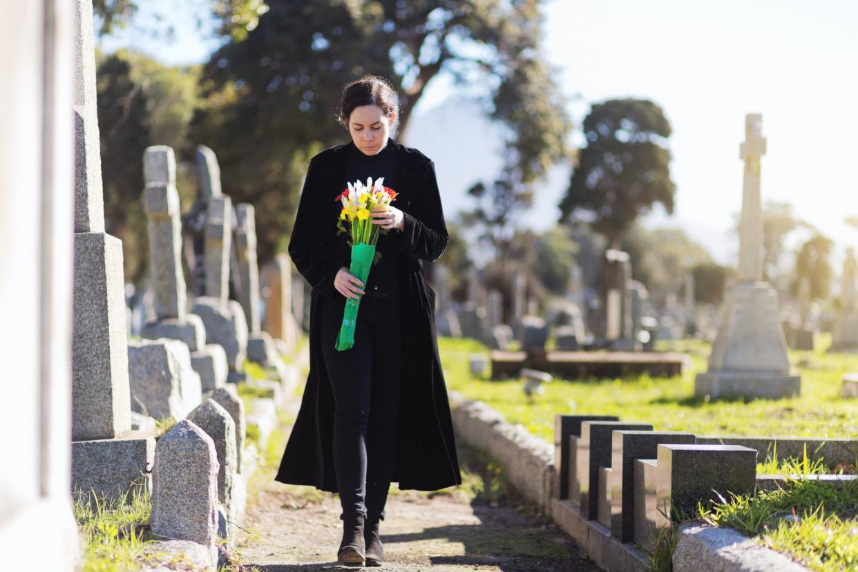 bereaved young woman in black taking flowers to grave