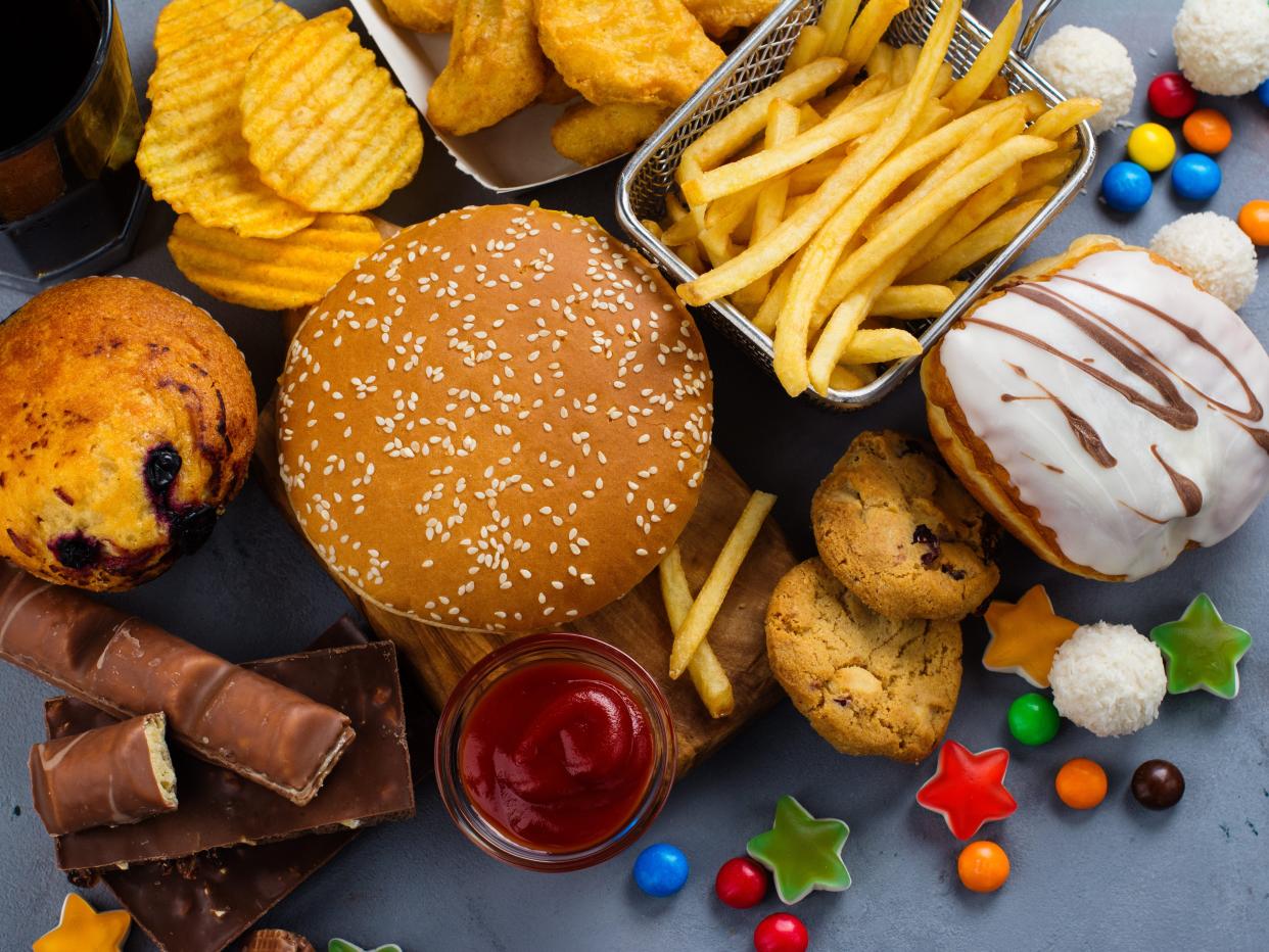 A pile of junk food including a burger, fries, chocolate and cookies.