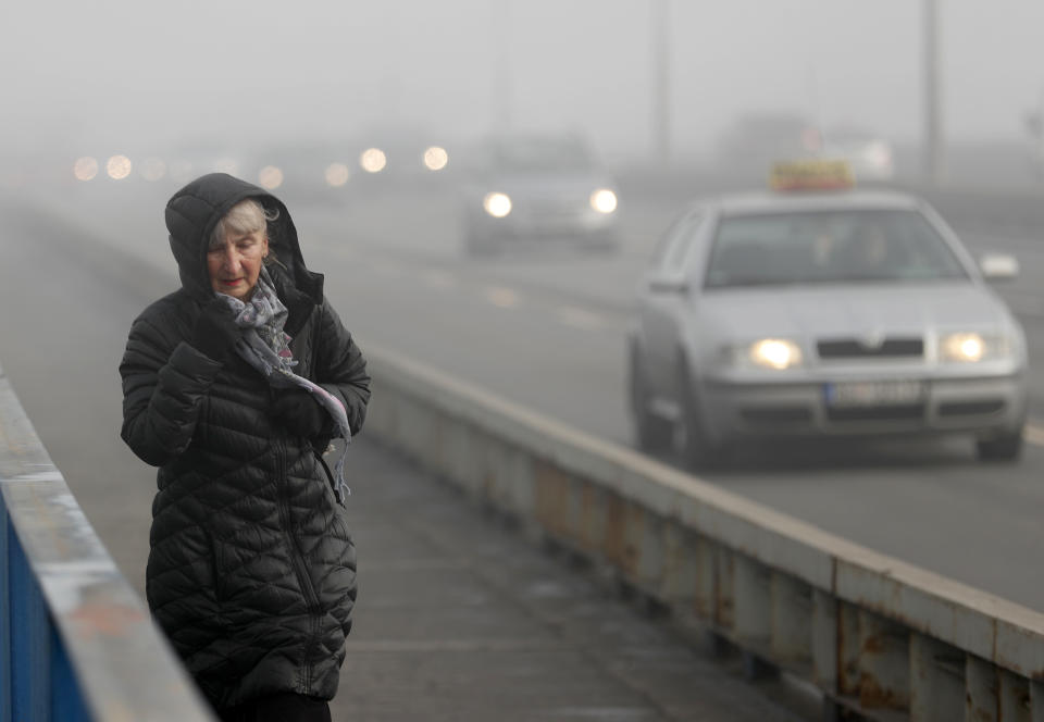 A woman walks across a busy bridge in Belgrade, Serbia, Wednesday, Jan. 15, 2020. Serbia's government on Wednesday called an emergency meeting, as many cities throughout the Balkans have been hit by dangerous levels of air pollution in recent days, prompting residents' anger and government warnings to stay indoors and avoid physical activity. (AP Photo/Darko Vojinovic)