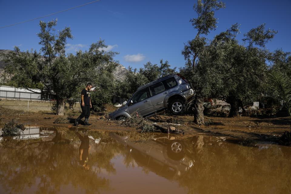 A man walks past a car moved by the force of flood water after storms in Kineta village, about 68 Kilometers (42 miles) west of Athens, Monday, Nov. 25, 2019. Authorities in Greece say two people have died and hundreds of homes have been flooded following an overnight storm that affected areas west of Athens. (AP Photo/Petros Giannakouris)