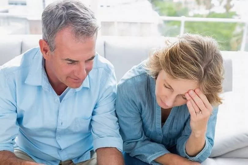 An older man and woman are studying paperwork with a worried look on their faces