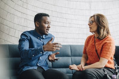 Two people have a conversation on a couch.