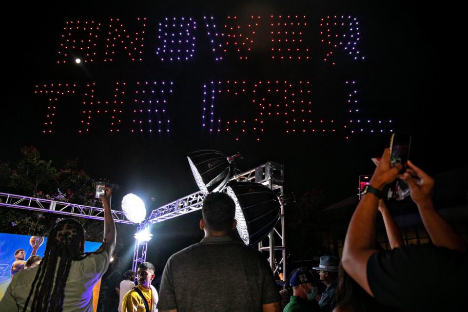 People watch lighted drones spell out "Answer the call"