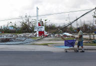 <p>A man pushes a shopping cart past downed cables after Hurricane Maria hit the island in September, in Humacao, Puerto Rico, Oct. 20, 2017. The writing in the back reads “Puerto Rico will rise.” (Photo: Alvin Baez/Reuters) </p>