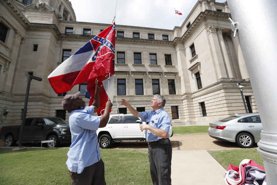 Mississippi Department of Finance and Administration employees Willie Townsend, left, and Joe Brown, raise a couple of Mississippi state flags over the Capitol grounds in Jackson, Miss., Tuesday, June 30, 2020. The two men raised and lowered about 100 flags, provided by the Secretary of State's office, for people or organizations that purchased a state flag that flew over the grounds. Gov. Tate Reeves will sign a bill Tuesday evening retiring the last state flag with the Confederate battle emblem during a ceremony at the Governor's Mansion. Upon the governor signing the bill, the flag will lose its official status. (AP Photo/Rogelio V. Solis)