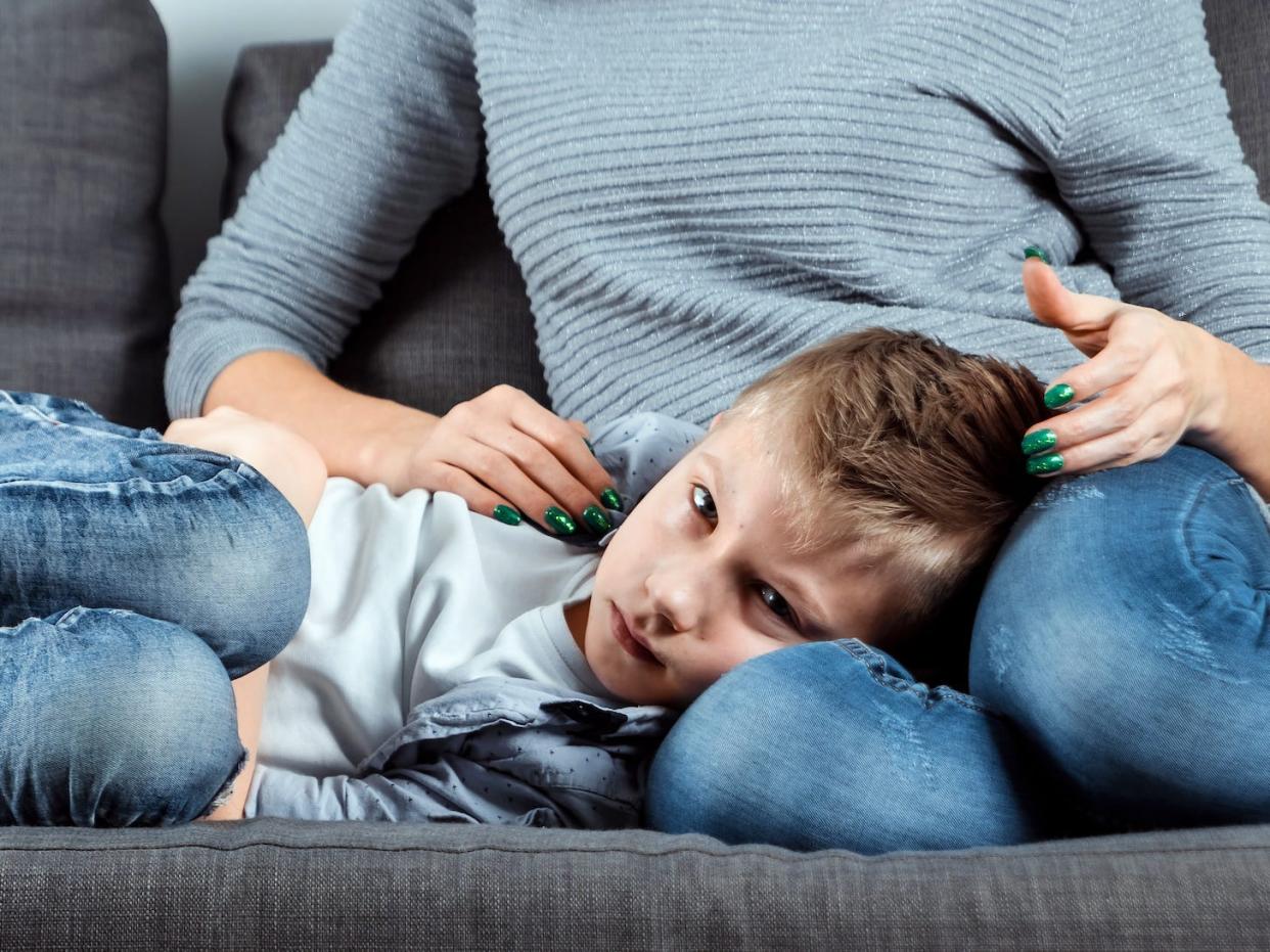 kid feeling sick on couch, being comforted by mom