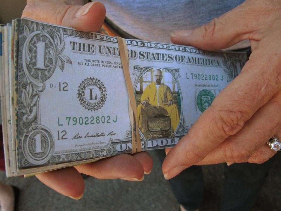 In this Aug. 9, 2013, photo an Albuquerque film liaison holds a "Walter White dollar" as tourist officials get ready for an event celebrating the premiere of the final season of AMC television series "Breaking Bad." The show was filmed in Albuquerque and has sparked interests in this Southwestern city from tourists. (AP Photo/Russell Contreras)