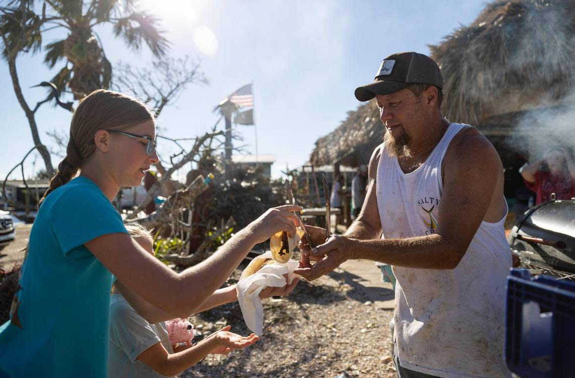 Johnny Smith, 49, the owner of Low Key Tiki, gives Cay Stevens, 13, and Marina Stevens, 6, food outside of his restaurant on Friday, Sept. 30, 2022, in St. James City, Fla. The local American Legion post donated their food for a community cookout. Hurricane Ian made landfall on the coast of South West Florida as a category 4 storm Tuesday afternoon leaving areas affected with flooded streets, downed trees and scattered debris.