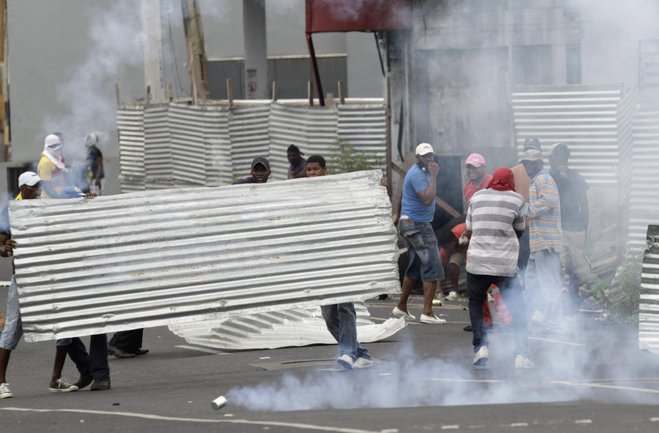 Demonstrators use a metallic sheet as a shield to cover from tear gas canisters fired by police officers during a protest in downtown Colon, Panama, Tuesday, Oct. 23, 2012. Demonstrators protested over a new law allowing the sale of state-owned land in the duty-free zone next to the Panama Canal. Protesters said the land is already being rented and it makes no sense to sell it. They said the government should instead raise the rent and invest the money in Colon, a poor and violent city. (AP Photo/Arnulfo Franco)