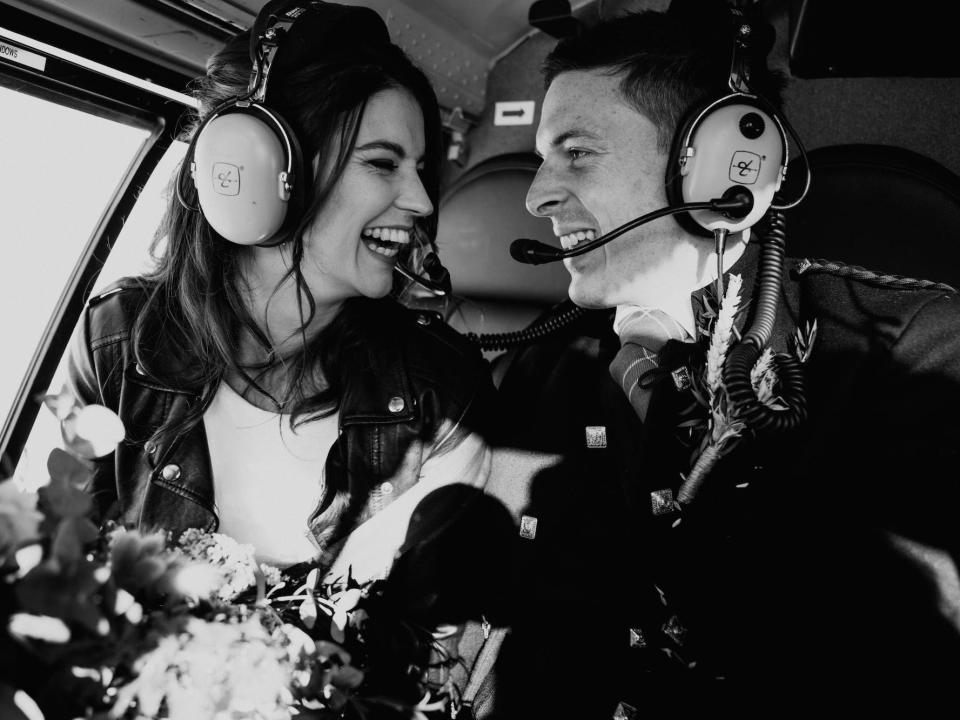 A bride and groom look at each other and laugh in a helicopter.