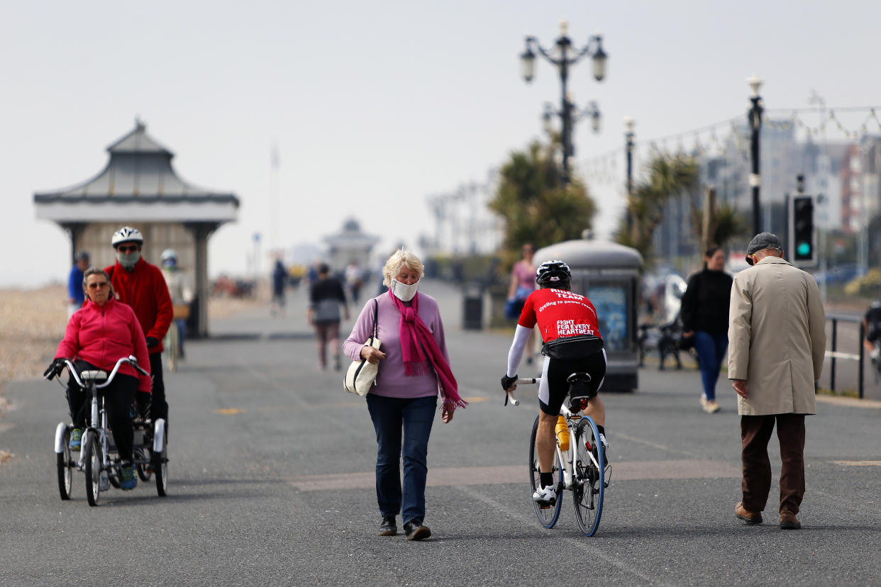 A woman in a protective mask walks past other people walking and cycling along Worthing promenade as the UK continues in lockdown to help curb the spread of the coronavirus.