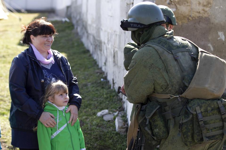 A Ukrainian girl looks at military personnel, believed to be Russian servicemen, standing outside the territory of a Ukrainian military unit in the village of Perevalnoye outside Simferopol March 3, 2014. Ukraine mobilised for war on Sunday and Washington threatened to isolate Russia economically after President Vladimir Putin declared he had the right to invade his neighbour in Moscow's biggest confrontation with the West since the Cold War. Russian forces have already bloodlessly seized Crimea, an isolated Black Sea peninsula where Moscow has a naval base. REUTERS/Baz Ratner (UKRAINE - Tags: POLITICS CIVIL UNREST)