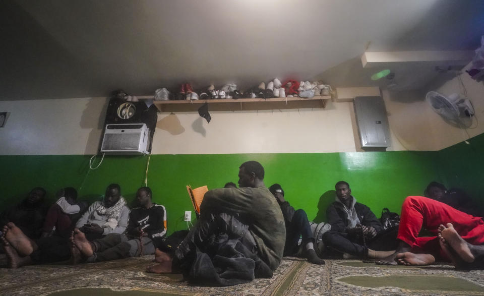 A Senegalese migrant, center, reads the Qurʾān following morning prayers, while other African migrants rest inside the main prayer area in the basement at Bronx's Masjid Ansaru-Deen mosque, Friday March 15, 2024, in New York. The mosque, formerly the family home for its Imam Omar Niass, has served as a temporary shelter and refuge since 2020 for hundreds of African migrants, while seeking asylum in the United States. (AP Photo/Bebeto Matthews)