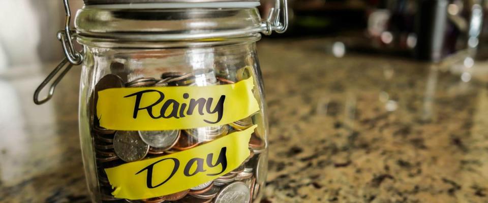 clear glass filled with coins that says rainy day denoting an emergency fund