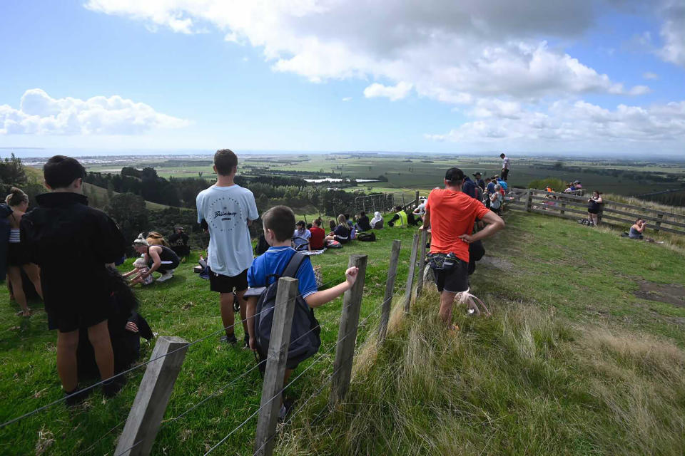 People watch for signs of a tsunami from a hill above Papamoa Beach, New Zealand, as a tsunami warning is issued Friday, March 5, 2021. A powerful earthquake struck in the ocean off the coast of New Zealand prompting thousands of people to evacuate and triggering tsunami warnings across the South Pacific. (George Novak/New Zealand Herald via AP)