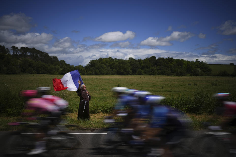 A man in a monk's robe waves the French flag as the peloton passes during the sixth stage of the Tour de France cycling race over 163.5 kilometers (101.6 miles) with start in Macon and finish in Dijon, France, Thursday, July 4, 2024. (AP Photo/Daniel Cole)