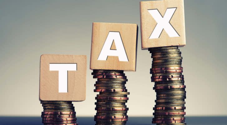 Stacks of coins hold up wooden blocks that spell out "TAX."