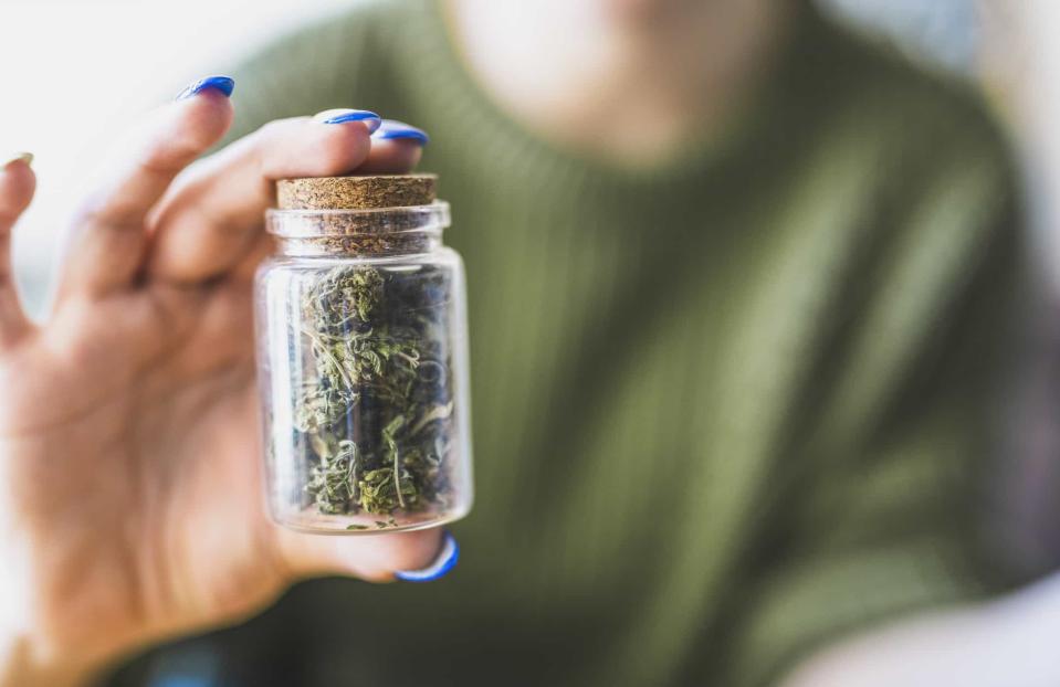 A person holds a small glass jar of marijuana.