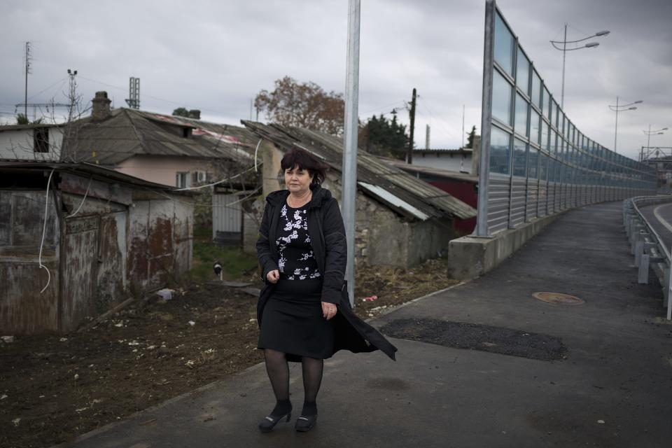 In this photo taken on Wednesday, Nov. 27, 2013, Irina Kharchenko walks away from her house beside the screen separating the yard of her house and a federal highway in the village Vesyoloye outside Sochi, Russia. As the Winter Games are getting closer, many Sochi residents are complaining that their living conditions only got worse and that authorities are deaf to their grievances. (AP Photo/Alexander Zemlianichenko)