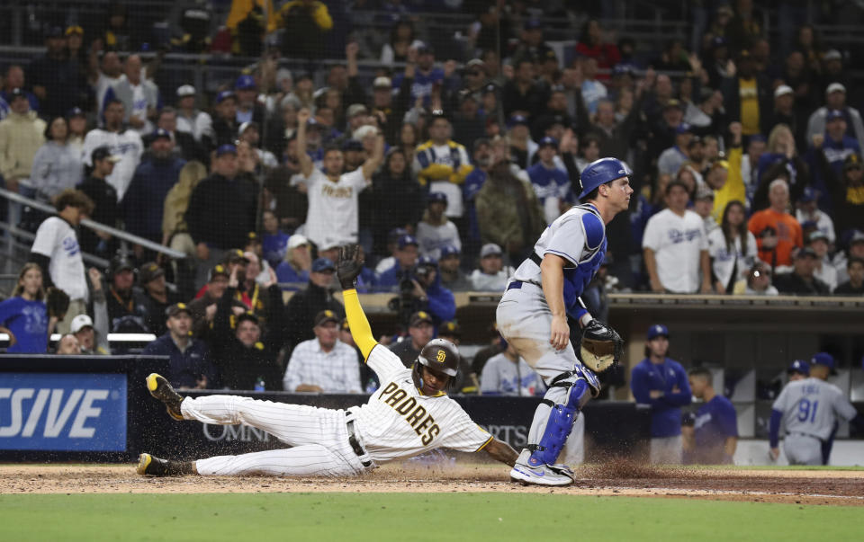 San Diego Padres' C.J. Abrams, left, scores the winning run on an Austin Nola sacrifice fly, next to Los Angeles Dodgers catcher Will Smith during the 10th inning of a baseball game Saturday, April 23, 2022, in San Diego. (AP Photo/Derrick Tuskan)