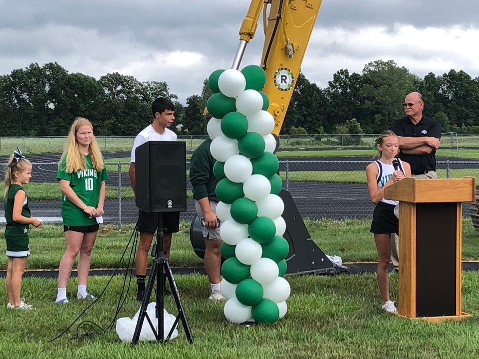 Senior cross country runner Sarah Koker addresses the crowd at the groundbreaking for the new Northridge Viking Stadium on Tuesday evening, as athletic director Kevin Jarrett looks on and other athletes await their turn.