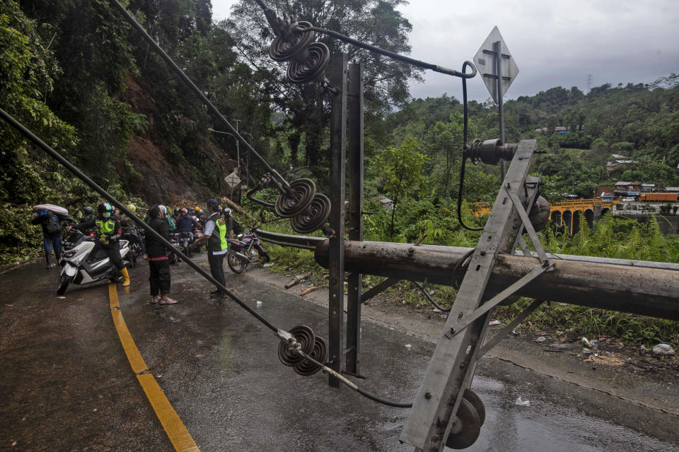 Motorists stop near an electricity pole fell down during an earthquake in Mamuju, West Sulawesi, Indonesia, Saturday, Jan. 16, 2021. Damaged roads and bridges, power blackouts and lack of heavy equipment on Saturday hampered Indonesia's rescuers after a strong and shallow earthquake left a number of people dead and injured on Sulawesi island. (AP Photo/Yusuf Wahil)