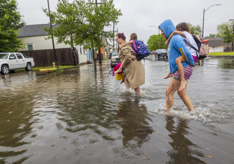 Tara Pledger and Rebecca Perez carry their daughters on their back as they walk across a flooded street in New Orleans, on Wednesday, April 10, 2024. Perez's home had two-feet of water in it so her friend, Tara, offered to help her get out. (Chris Granger/The Times-Picayune/The New Orleans Advocate via AP)