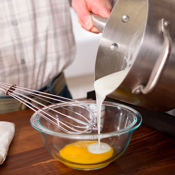 A person carefully pouring some of the mixture into a bowl of egg yolk