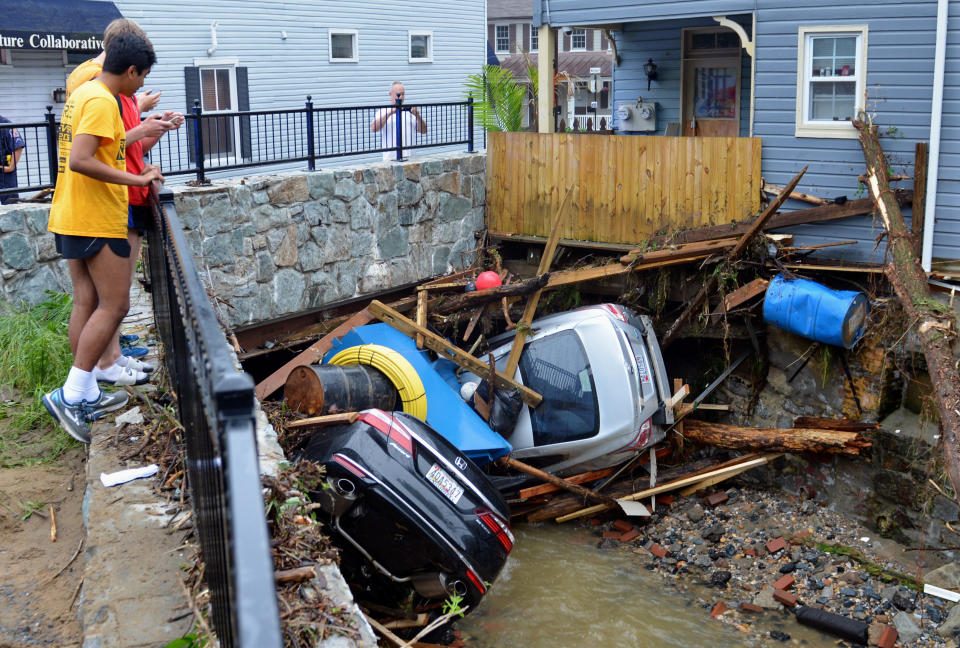 <p>Residents gather by a bridge to look at cars left crumpled in one of the tributaries of the Patapsco River that burst its banks as it channeled through historic Main Street in Ellicott City, Md., Monday, May 28, 2018. (Photo: David McFadden/AP) </p>