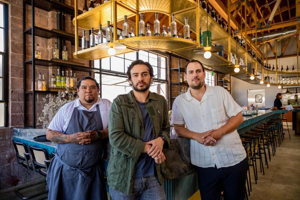 Three men lean against a restaurant bar